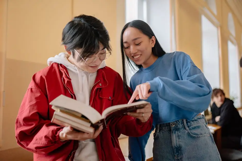 Two students collaborating by looking at a book together with a classroom setting in the background.