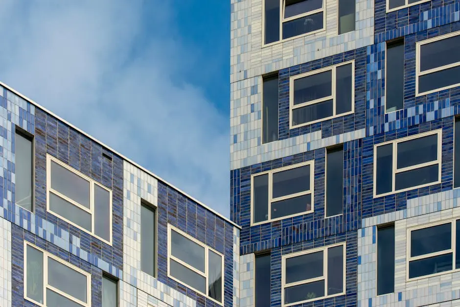 Close-up of a contemporary building facade with reflective glass windows against a blue sky with clouds.